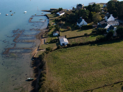 Paysage littoral de Crac’h dessiné par l’activité ostréicole (terre-pleins, cabanes et bassins). En arrière-plan, apparaît la cale et le môle de Fort Espagnol. Coastal landscape of Crac'h designed by the oyster farming activity (platforms, huts and basins). In the background, the hold and the quay of Fort Espagnol appear.